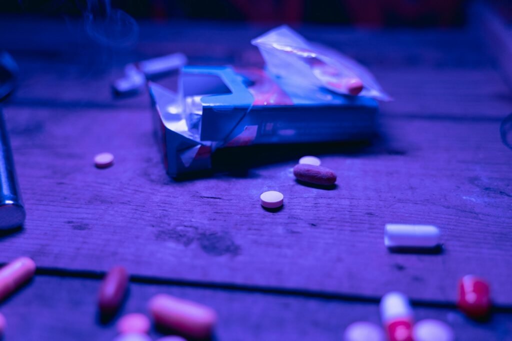 Various pills scattered on a wooden table under purple light, depicting medication or substance concept.